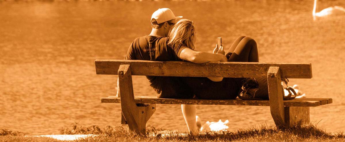 Junge Frau und Mann entspannen auf einer Bank am See.